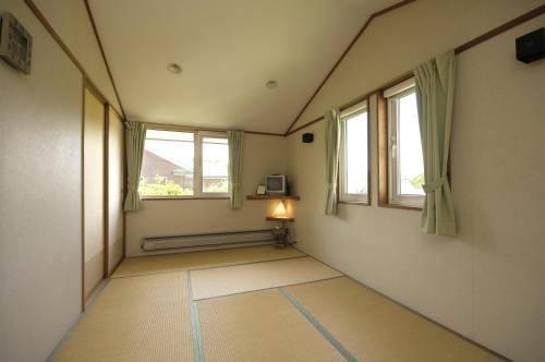 um quarto vazio com duas janelas e um candeeiro em Pension Field em Hokuto