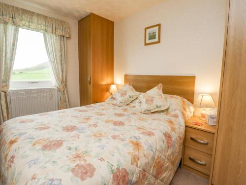 a bedroom with a bed with a floral bedspread and a window at New Cottage in Wooler