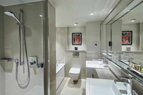 a bathroom with two sinks a toilet and a shower at London Marriott Hotel Kensington in London