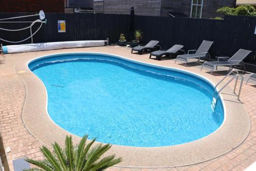 a large blue swimming pool with chairs in a yard at Calendo Apartments in Merimbula