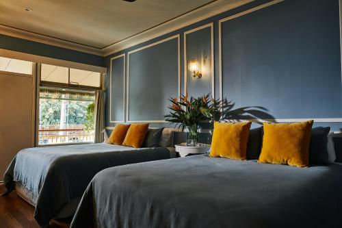 2 camas en una habitación con paredes azules y almohadas amarillas en Eltham Hotel NSW, en Eltham