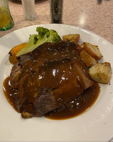 um prato de carne com molho, brócolos e batatas em Walwa Hotel 