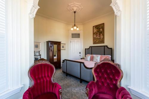 a bedroom with a bed and two red chairs at Pinc Lady Mansion in Eureka