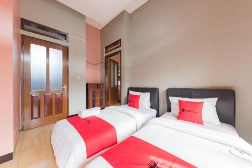 two beds in a room with red pillows at RedDoorz Syariah near Politeknik Negeri Bandung Campus in Bandung