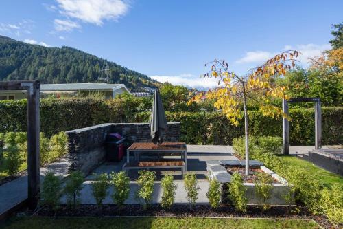 a garden with an umbrella and a table and bench at Pinewood Queenstown in Queenstown