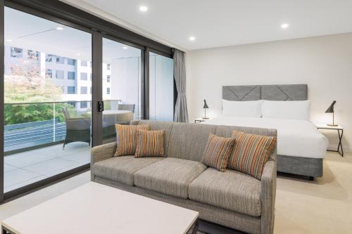 Meriton Suites Canberra في كانبرا: غرفة نوم بسرير واريكة وسرير