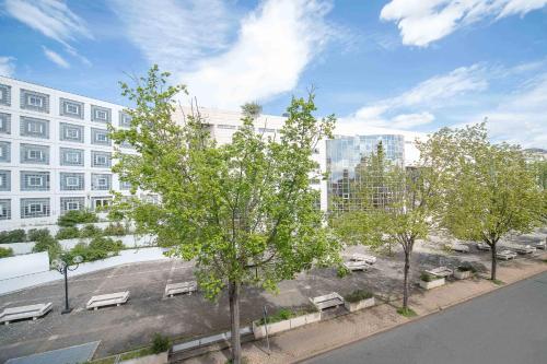 un parc avec bancs et arbres devant un bâtiment dans l'établissement Résidence Bains Callou située face aux thermes, à Vichy