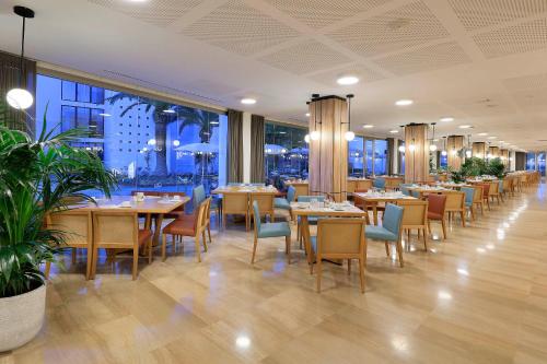 a restaurant with wooden tables and chairs and windows at Grand Palladium Select Palace Ibiza - All Inclusive in Playa d'en Bossa