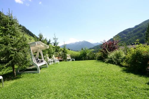 a yard with white chairs and mountains in the background at Hotel Alpenfrieden in Rio Bianco