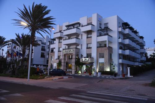 un bâtiment blanc avec un palmier en face dans l'établissement Golden Beach Appart'hotel, à Agadir