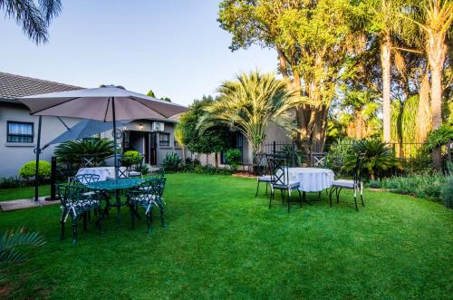 a yard with tables and chairs and an umbrella at Three Olives Guesthouse in Centurion
