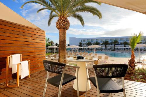 a deck with a palm tree and a table and chairs at Grand Palladium Palace Ibiza Resort & Spa- All Inclusive in Playa d'en Bossa