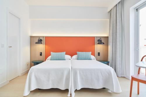 a bedroom with a large white bed with an orange headboard at Excelsior Estudios & Apartamentos in San Antonio