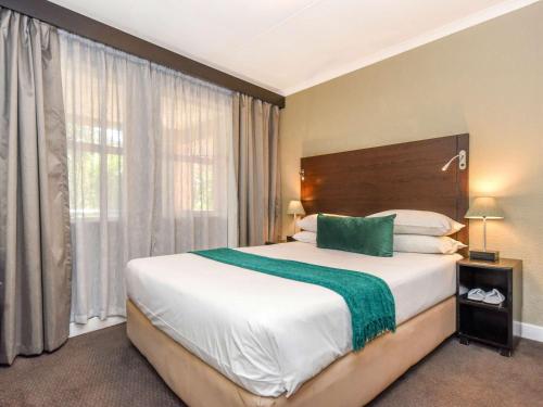 um quarto com uma cama grande e uma janela grande em Mercure Hotel Bedfordview em Joanesburgo