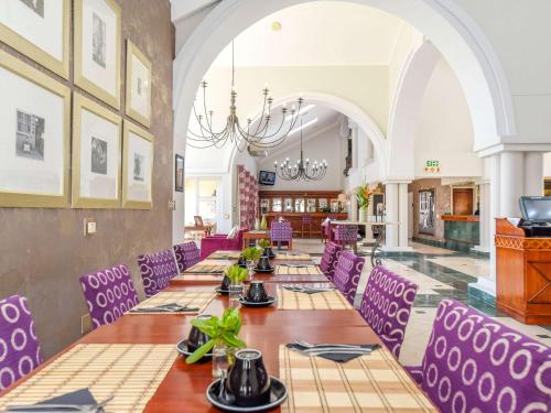 a long dining room with purple chairs and tables at Mercure Johannesburg Randburg in Johannesburg
