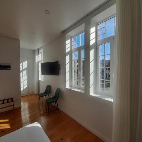 a room with three windows and two chairs and a television at DOURO B&B Avenida in Resende