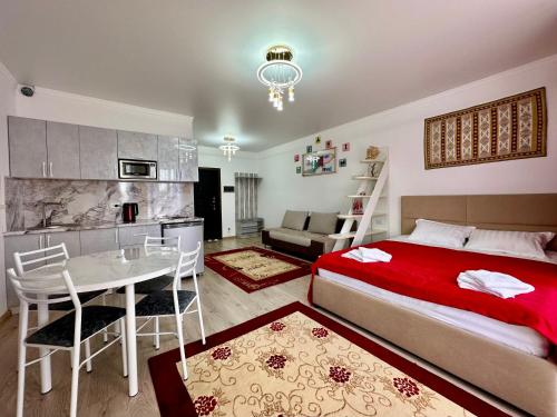 a bedroom with a bed and a table and a kitchen at Raduga West 'Amber' Apartment in Koshkolʼ