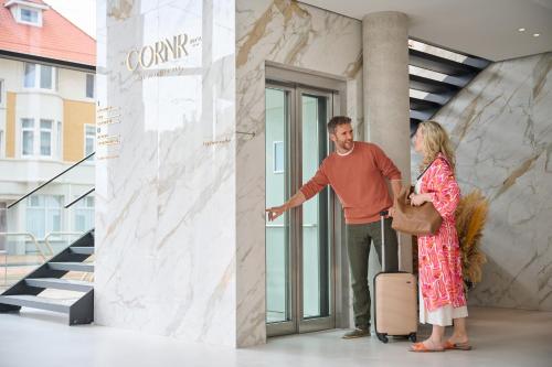 a man and a woman with a suitcase in front of a building at The CORNR Hotel in Nieuwpoort