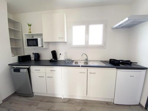 a white kitchen with a sink and a microwave at Auberge des Plaines - Appartements avec terrasse in Arles