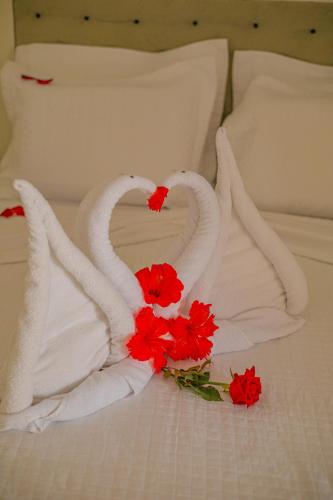 two towel swans on a bed with red flowers at Pousada Polymar in Maragogi