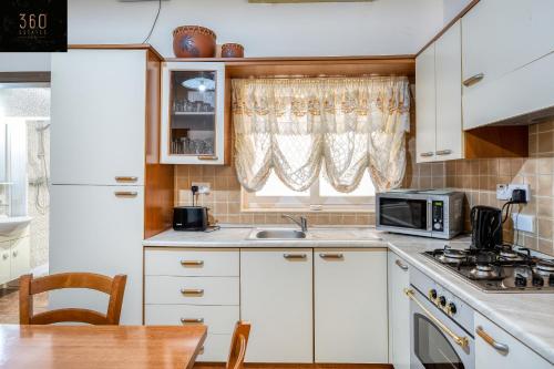een keuken met witte kasten, een wastafel en een magnetron bij Lovely, comfy 2BR home with comfy sofa w/WIFI & AC by 360 Estates in St Paul's Bay