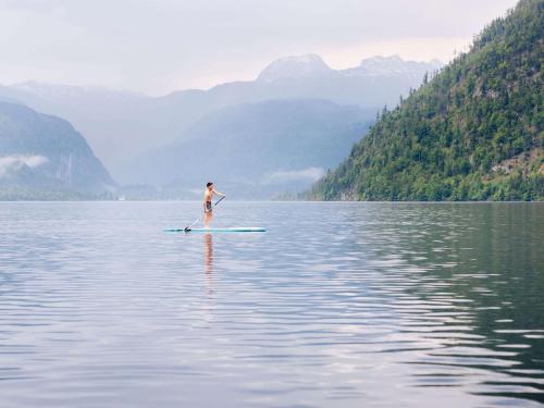 a man standing on a paddle board in the water at TAUROA Seehotel Grundlsee in Grundlsee