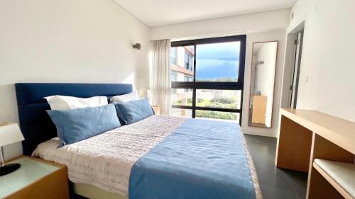 een slaapkamer met een blauw bed en een groot raam bij Troia Garden View Apartment in Troia