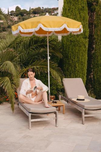 a woman sitting in a chair under an umbrella at Les Terrasses du Bailli in Rayol-Canadel-sur-Mer
