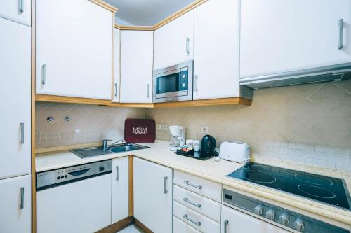 a kitchen with white cabinets and a sink and a microwave at Grand Muthu Forte do Vale in Albufeira