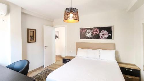 1 dormitorio con cama blanca y lámpara de araña en Playa El Palo Apartment by SharingCo, en Málaga