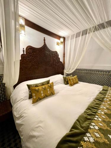 a bedroom with a large white bed with gold pillows at Le Grand Alcazar - Riad in Fès