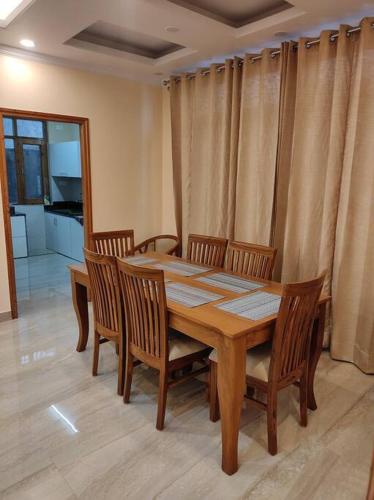 a wooden dining room table and chairs with curtains at Superb Luxury Three Bed Apartment in Shimla
