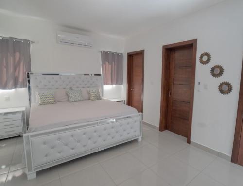 a white bedroom with a large bed and a wooden door at Villa Golden Dream in San Felipe de Puerto Plata