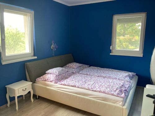 a bedroom with a bed with a blue wall and two windows at Pentz House in Siófok