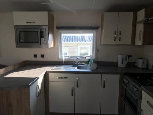 a kitchen with white cabinets and a sink and a window at Lovely Holiday Caravan, great location - Pebble Bank, near Chesil Beach in Wyke Regis