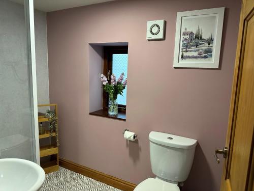 a bathroom with a toilet and a vase of flowers at Old Post Office Barn in Leek