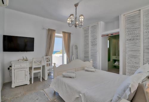 a white bedroom with a bed and a desk and a television at Villa Yialos in Antiparos Town