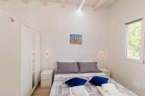 biała sypialnia z łóżkiem z niebieskimi poduszkami w obiekcie Perladelmare w mieście Avola
