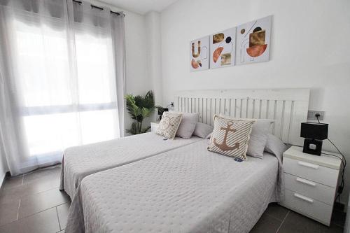 a white bedroom with two beds and a window at Apartamento Bajo 1 Marjal playa centro de Guardamar in Guardamar del Segura