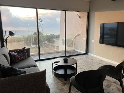 a living room with a couch and a table and a large window at דירת גן על הים בנהריה in Nahariyya