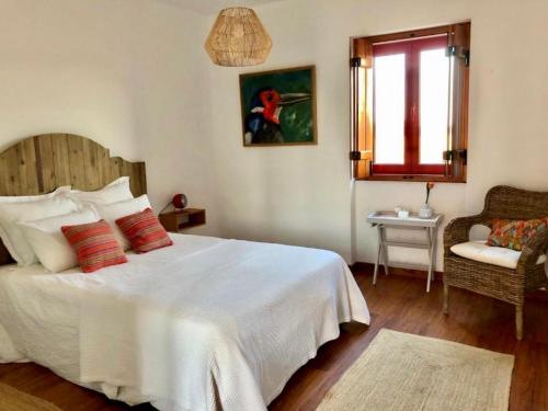 1 dormitorio con cama blanca, ventana y silla en Herdade da Burquilheira, en Alcáçovas