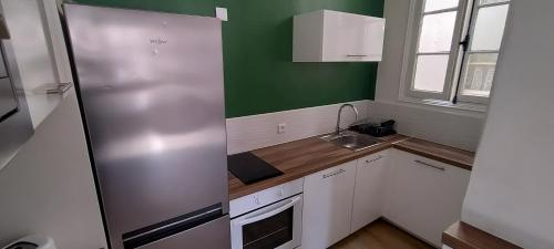 Elle comprend une petite cuisine avec des placards blancs et un mur vert. dans l'établissement Appartement ensoleillé, à Perpignan