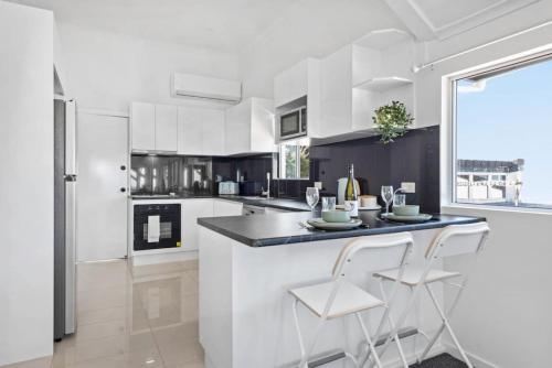 uma cozinha com armários brancos e um balcão com dois bancos em Bay Vista Two Bedroom Waterfront Apartment em Redcliffe