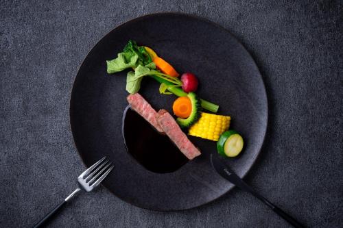 a black plate of food with meat and vegetables at Holiday Inn Resort Shinano-Omachi Kuroyon by IHG in Omachi