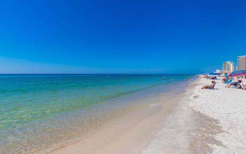 a beach with people sitting on the sand and the water at Phoenix All Suites West Hotel in Gulf Shores