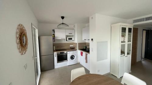 - une cuisine avec des appareils blancs, une table et des chaises dans l'établissement Calvi 2 pièces NEUF - vue mer piscine 18 m - proche plage - location par semaine complète, à Calvi