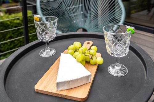 a table with two wine glasses and a block of cheese and grapes at Rytas cozy apartment in the guest house with the terrace and the stunning view to the river side in Birštonas