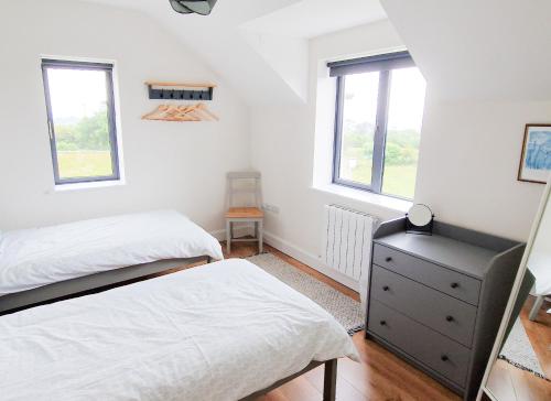 a bedroom with two beds and a dresser and two windows at Bell View Holiday Home Sheeps Head by Trident Holiday Homes in Bantry