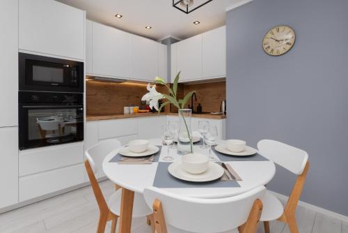 a white kitchen with a table and chairs and a clock at Stunning Apartment Hokejowa with Terrace & Parking by Renters in Gdańsk
