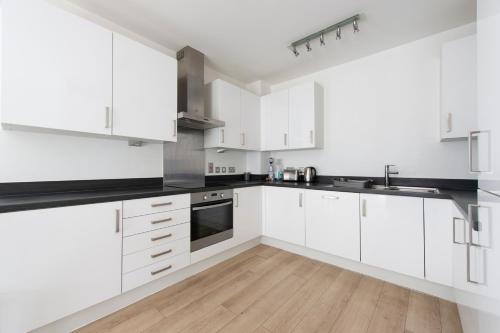 cocina blanca con armarios blancos y suelo de madera en Luxury Apartment Canning Town en Londres